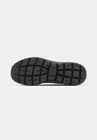 Black rubber shoe sole with a textured surface, featuring a tread pattern of squares and grooves for grip and traction.