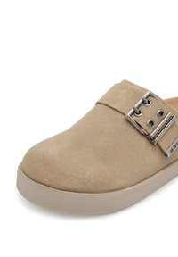 Beige velúr cipő kerek orral, széles pánttal és ezüst csattal. Texturált felsőrésze van, valamint lapos, világos színű talpa.