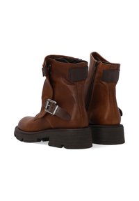 Hnědé kožené kotníkové boty s kulatou špičkou, bočním zipem a nastavitelným popruhem s přezkou. Texturovaná podrážka pro trakci a stabilitu.
