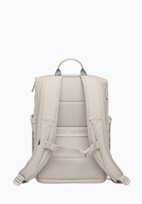 Sac à dos beige avec un dos et des bretelles rembourrés, comprenant une poignée supérieure, des poches latérales et un texte en relief "CRÉER UN IMPACT".