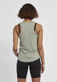 Ljust grön atletisk linnetopp med nättyg och en avslappnad passform, lagd över svarta sportshorts med vita detaljer.