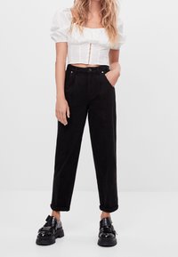 Black high-waisted trousers with side pockets and a relaxed fit. Paired with a white puff-sleeve crop top, highlighting a square neckline.