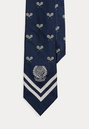 Cravate bleu marine avec un motif répétitif de paires de raquettes de tennis blanches, deux bandes diagonales argentées près de la pointe, et un emblème sur le thème de Wimbledon.