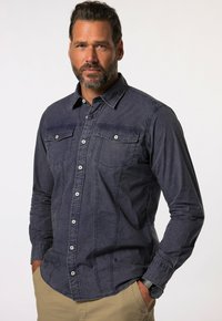 Donkerblauwe denimshirt met lange mouwen, borstzakken en drukknopen. Bevat subtiele stikseldetails en een ontspannen pasvorm.