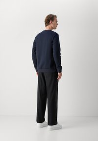 Marinblå sweatshirt med rund halsringning, ribbad mudd och nederkant, i kombination med svarta byxor och vita sneakers. Minimalistisk design, inga synliga mönster.