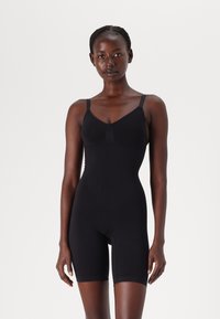 Svart bodysuit med justerbara axelband, sömlös design och mid-thigh längd. Tillverkad av elastiskt material för en åtsittande silhuett.