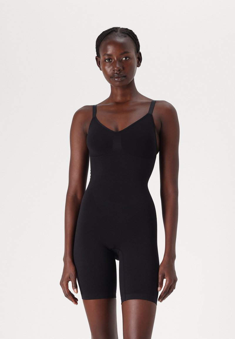 Svart bodysuit med justerbara axelband, sömlös design och mid-thigh längd. Tillverkad av elastiskt material för en åtsittande silhuett.