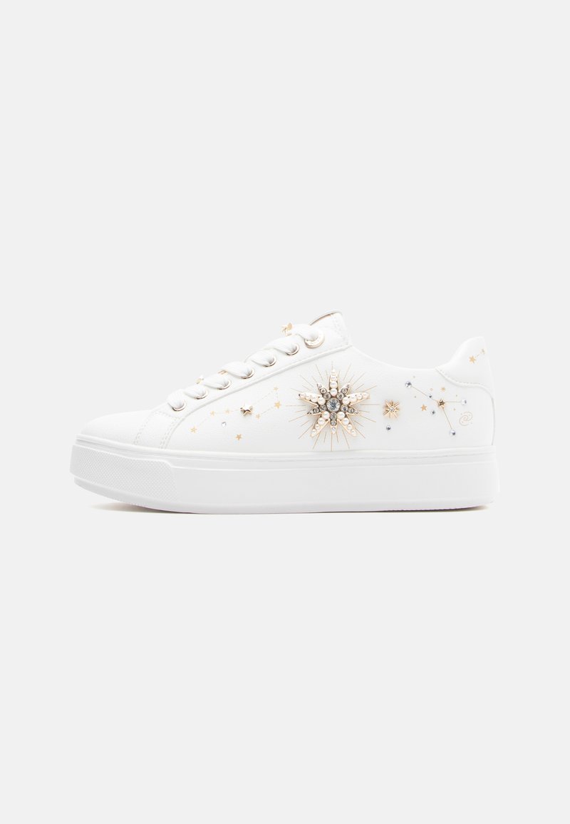Zapatilla deportiva de lona blanca con detalles metálicos, un diseño de explosión de estrellas adornado con joyas y pequeños patrones de estrellas doradas, con una suela de goma plana.