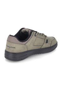 Zapatilla verde de ante con suela de goma negra, que presenta detalles perforados, cierre con cordones y marca en el talón.