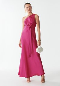 Viena peties, fuksijų spalvos suknelė su mazgo juosmens dizainu, plaukiantis siluetas ir lygus paviršius. Derinama su balta, kriauklės formos rankine.