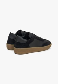 Schwarze Sneakers aus einer Mischung aus glattem Leder und Wildleder, mit einer Gummisohle und minimalistischer Gestaltung, die subtile Akzente und Nähte zeigt.