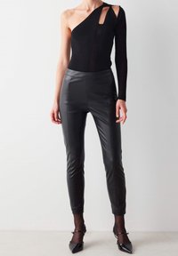 Svart enaxlad bodysuit med utskärning, i kombination med figurnära svarta läderbyxor med framsömmar och hög midja. Svarta klackar kompletterar looken.