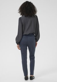 Dark gray textured blouse with long sleeves, paired with fitted navy pants. Black shoes visible, focusing on clothing design and color.