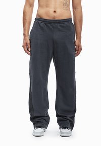 Donkergrijze joggingbroek van zacht materiaal, met elastische tailleband, zijstrepen en een losse pasvorm, gecombineerd met witte sneakers.