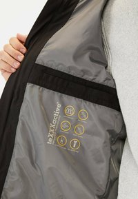 Veste noire avec un intérieur gris affichant des icônes étanches, respirantes et coupe-vent. Présente une membrane en matériau recyclé et des coutures thermocollées.