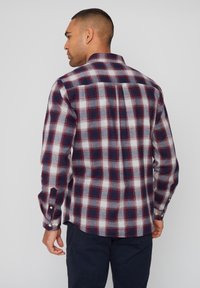 Camisa de franela en diseño de cuadros en azul marino, rojo y blanco. Textura suave, mangas largas, puños con botones y detalle de yugo trasero. Corte de dobladillo recto.