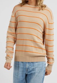 Beige trui met oranje horizontale strepen, geribbelde manchetten en zoom, gemaakt van een zachte brei. Draag met lichtblauwe jeans.