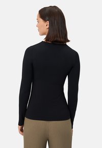 Černý dlouhý rukáv top vyrobený ze hladkého materiálu, s těsným střihem a kulatým výstřihem, spárovaný s žebrovanými béžovými kalhotami.