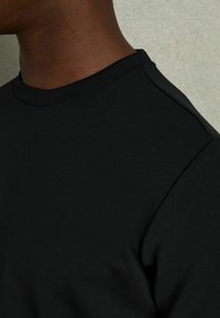 Camiseta de cuello redondo negra, fabricada con tejido suave, que presenta una forma ajustada con costuras mínimas y un escote suave.