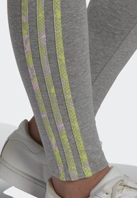 Pelēkas legingi ar dzīvām dzeltenām un rozā svītrām sānos, ar gludu tekstūru un pieguļošu dizainu.