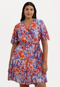 Cvetna obleka z zavihkom, ki prikazuje mešanico rdečih, oranžnih in modrih cvetov na svetli podlagi. Ima kratke flikarjeve rokave in pas z zavezo.