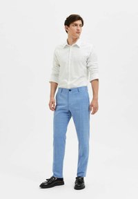 Ljusblå skräddarsydda byxor i ett texturerat tyg, matchade med en vit mönstrad skjorta. Ensemblet fullbordas med svarta skor.