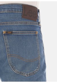 Jeans i denim i en medelblå tvätt med en brun läderetikett med präglad "Lee" på baksidan av midjan och kontrasterande sömmar på fickorna.