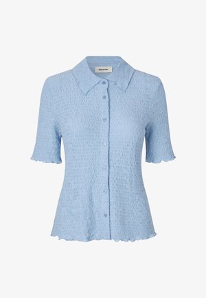 Lyseblå kortermet skjorte med en teksturert bølgete mønster, knappelukking, og scallopede kanter på nederste kant og ermer. Kragedesign.