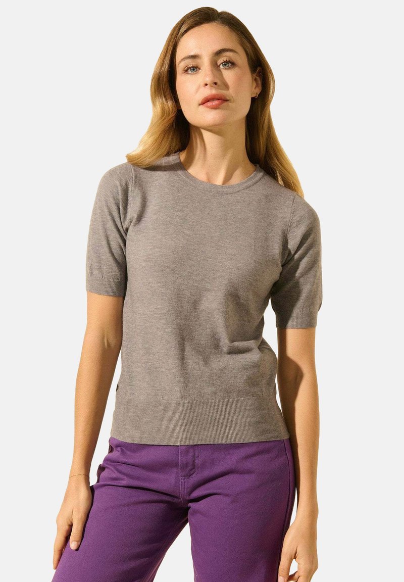 Pull en tricot gris clair à manches courtes avec un col rond, texture douce, design ajusté, associé à un pantalon violet pour un contraste.