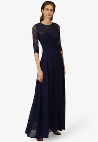 Abito da sera blu navy con corpino in pizzo decorato da motivi floreali, maniche a tre quarti e una gonna in chiffon fluida.