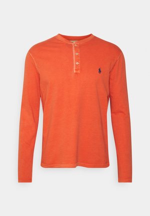Langarmhemd aus leuchtend orangefarbener Baumwolle mit Henley-Ausschnitt, drei Knöpfen und navyblauem Logodetail auf der linken Brust.