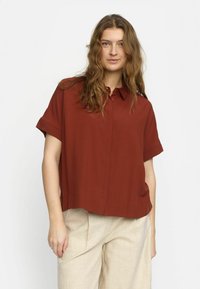 Rust-colored short-sleeve shirt with a collar, featuring a relaxed fit and button front, paired with light beige linen pants.