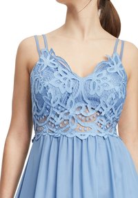 Světle modré šaty s krajkovým zdobením na korzetu, s nastavitelnými ramínky a splývavou sukní pod páskem. Měkká textura po celé ploše.