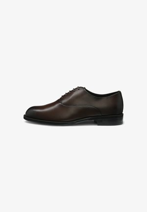 Scarpa oxford da uomo in pelle marrone scuro con allacciatura chiusa e tacco leggero su sfondo bianco.