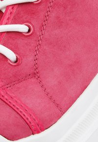 Zapatilla de ante rosa con cordones y ojetes blancos. Presenta costuras rosas y una superficie texturizada. Suela de goma con un borde blanco.