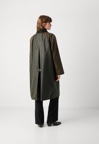 Olijfgroene, lange jas met een hoge kraag, relaxte pasvorm en knoopdetail aan de achterkant. Gemaakt van een glad, licht glanzend materiaal.