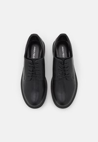 Chaussures en cuir noir avec un bout arrondi, un design à lacets, une semelle plate et des détails de surpiqûres subtils. Texture lisse avec un minimum d'ornements.