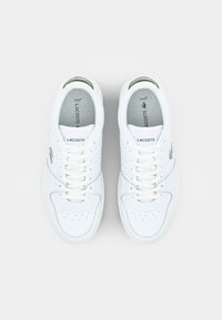 Witte leren sneakers met groene accenten, geperforeerd ontwerp en platte veters. Lacoste-logo gedrukt op de zijkant en de tong.