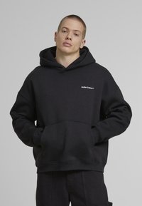 Black hooded sweatshirt made of cotton, featuring a front kangaroo pocket and embroidered logo on the chest. Loose fit and ribbed cuffs.