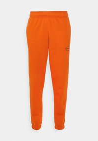 Orange sweatpants med elastisk midja och cuffar, tillverkade av mjukt tyg. Har en liten svart logotyp på vänster sida.