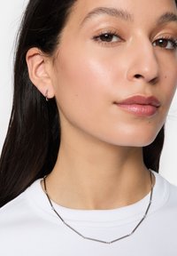 Collana d'argento con anelli geometrici allungati e piccoli accenti circolari. Il modello indossa una camicia bianca. Design minimalista e finitura lucida.