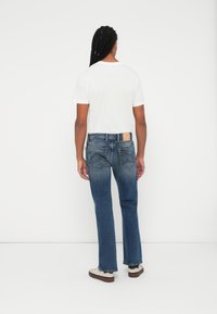 Μπλε τζιν παντελόνι με ίσια γραμμή, διαθέτει ανοιχτό χρώμα πλύσης, πίσω τσέπες με λεπτομέρεια ραφής και καφέ δερμάτινη παλέτα στη μέση.