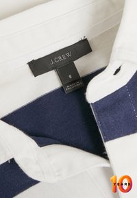 Valko- ja tummansiniraidallinen puuvillapolo, jossa on taitettu kaulus. Tunnuksessa lukee "J. Crew", koko "S" ja "Valmistettu Filippiineillä."