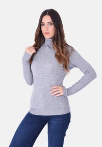 Maglione grigio a collo alto con maniche lunghe, polsini a costine e un design aderente, abbinato a jeans blu scuro. Stile semplice e classico.