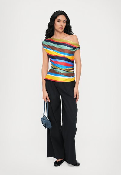 Kleurige off-the-shoulder top met horizontale strepen in groen, blauw, geel en bruin, gecombineerd met wijde zwarte broek en een denim tas.