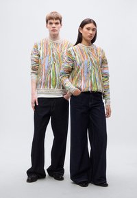 Πλεκτό πουλόβερ με πολύχρωμο αφηρημένο μοτίβο, με στρογγυλή λαιμόκοψη και ριμπ μανσέτες, συνδυασμένο με σκούρο τζιν φαρδιάς γραμμής.