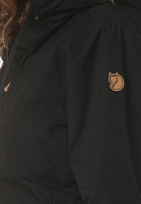 Čierna bunda vyrobená z vodeodolného materiálu; má zips, kapucňu a logo nášivku v tvare mačky z imitácie kože na ľavom pleci.