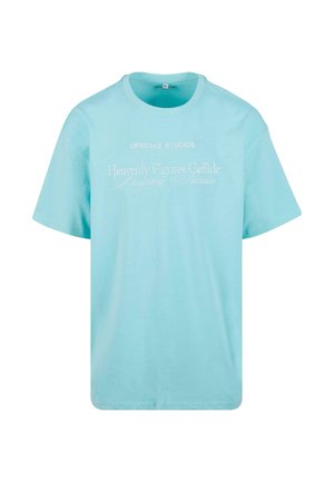 Svetlo modré bavlnené tričko s okrúhlym výstrihom, krátkymi rukávmi a potlačeným bielym textom, ktorý hovorí "UPSCAL STUDIOS" a "Nebeské postavy sa zrážajú."