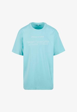 Világoskék pamut póló kerek nyakkal, rövid ujjú, nyomtatott fehér szöveggel, amely így szól: "UPSCAL STUDIOS" és "Heavenly Figures Collide."