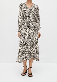 Robe portefeuille à manches longues en tissu beige à imprimé léopard noir, avec un décolleté en V et une jupe fluide, associée à des sandales noires à brides.